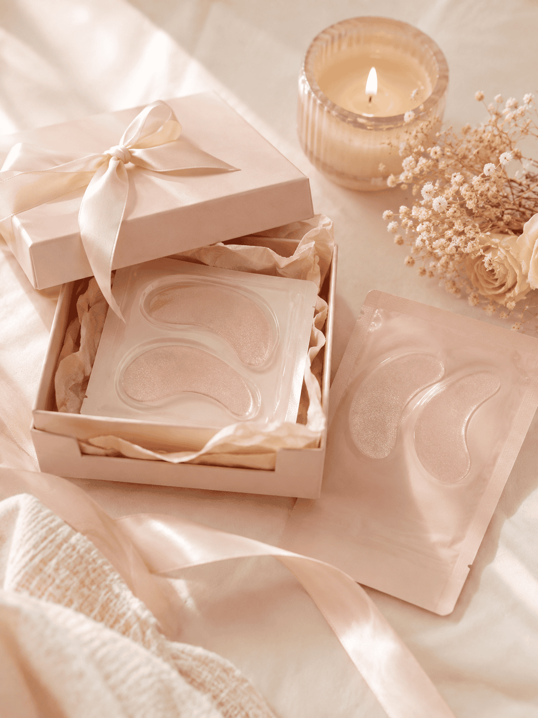 Under-eye patches in a pink gift box with candle and flowers
